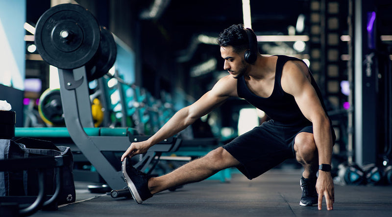 Young Indian man stretching before workout in gym while wearing headphones