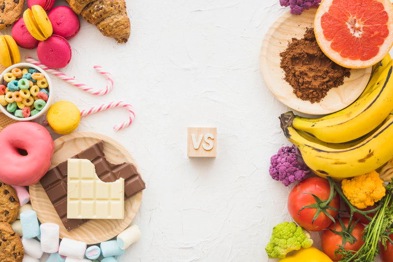 Comparison between unhealthy processed foods and fresh healthy fruits and vegetables on white background